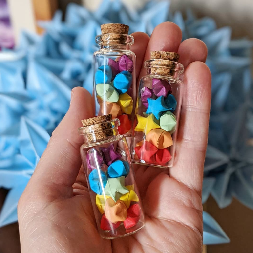 A hand holds tiny bottles of origami stars.