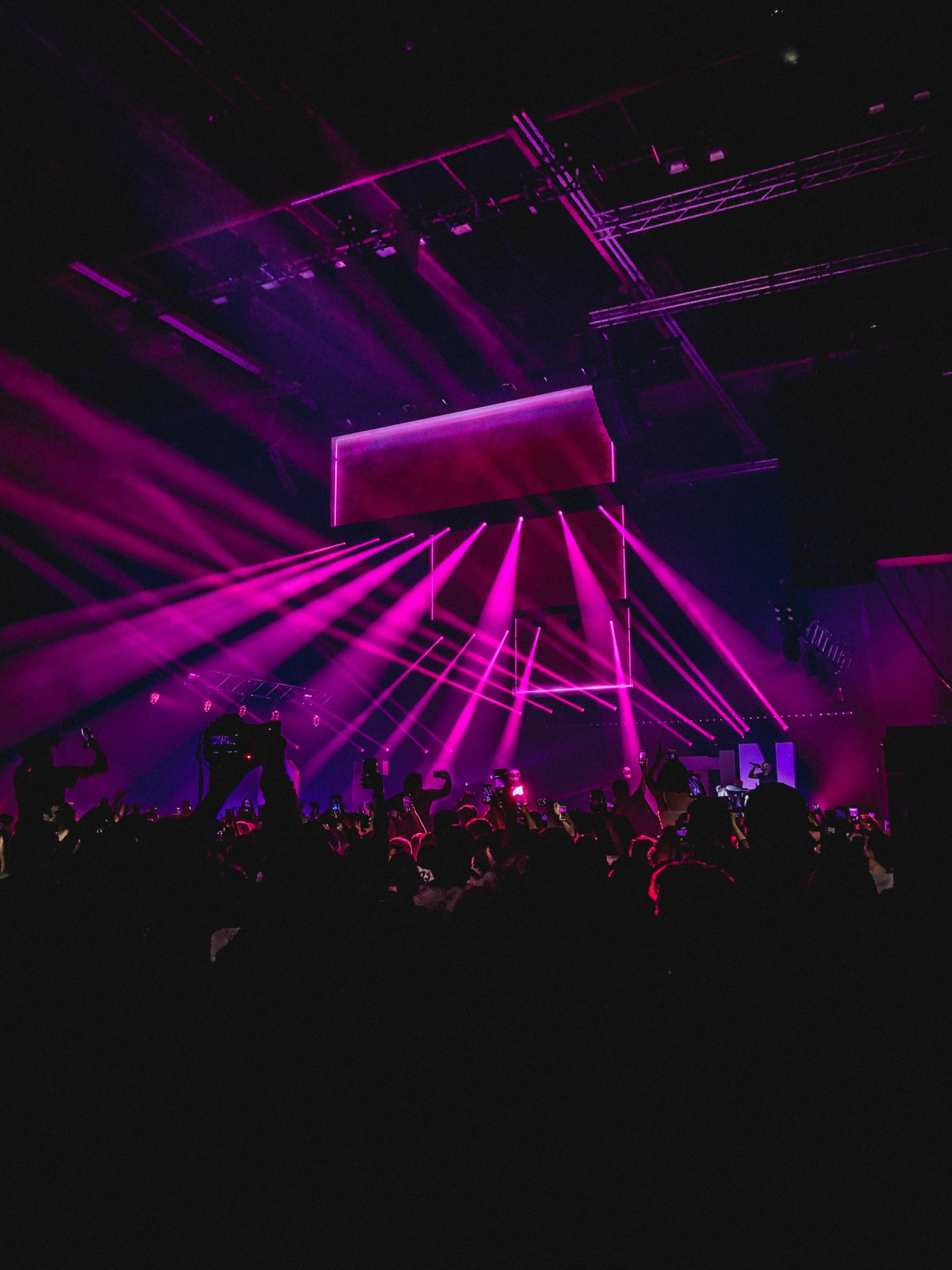 People performing onstage amongst a crowd with neon pink strobe lights highlighting the atmosphere.