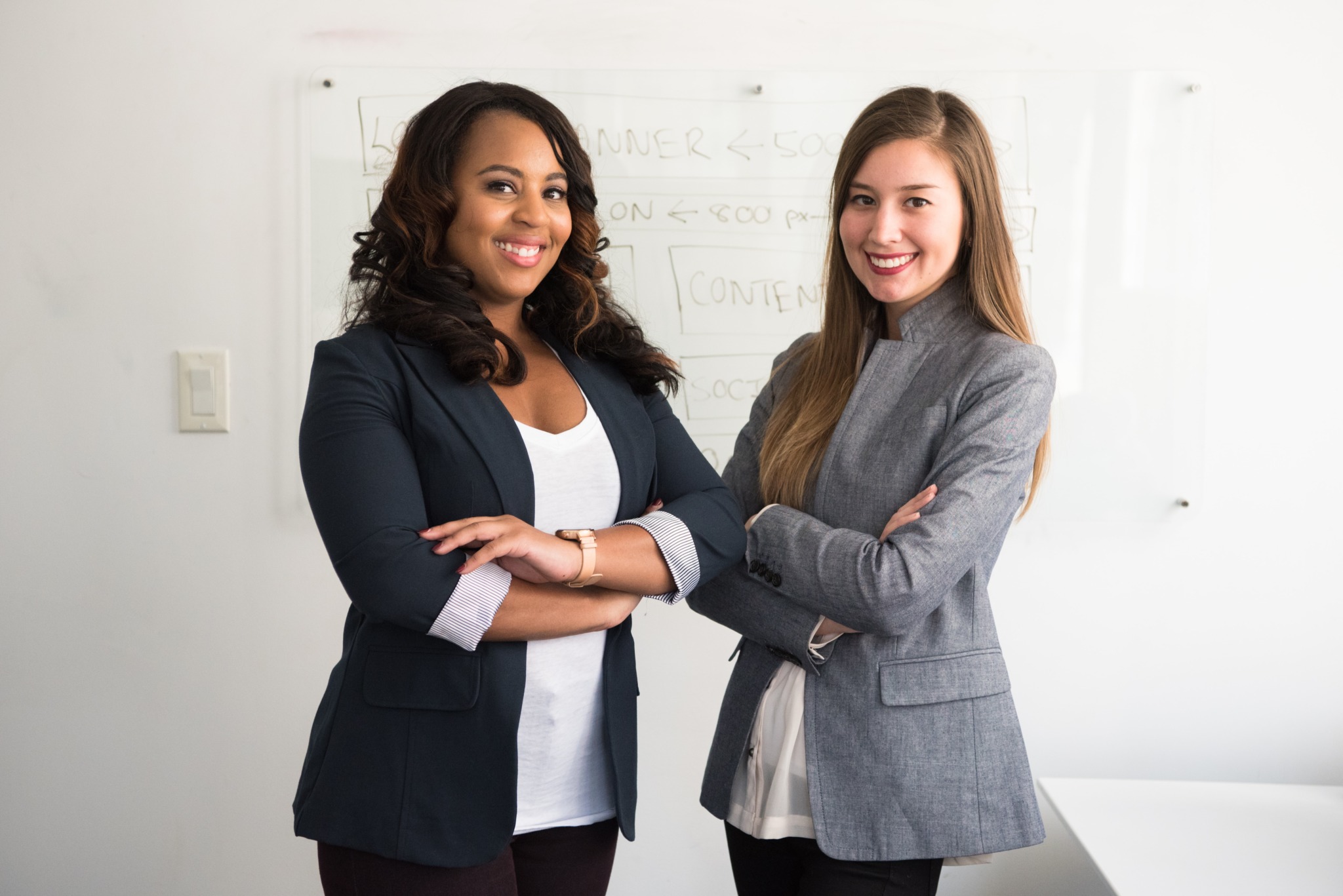 Two women in suits standing beside a wall.