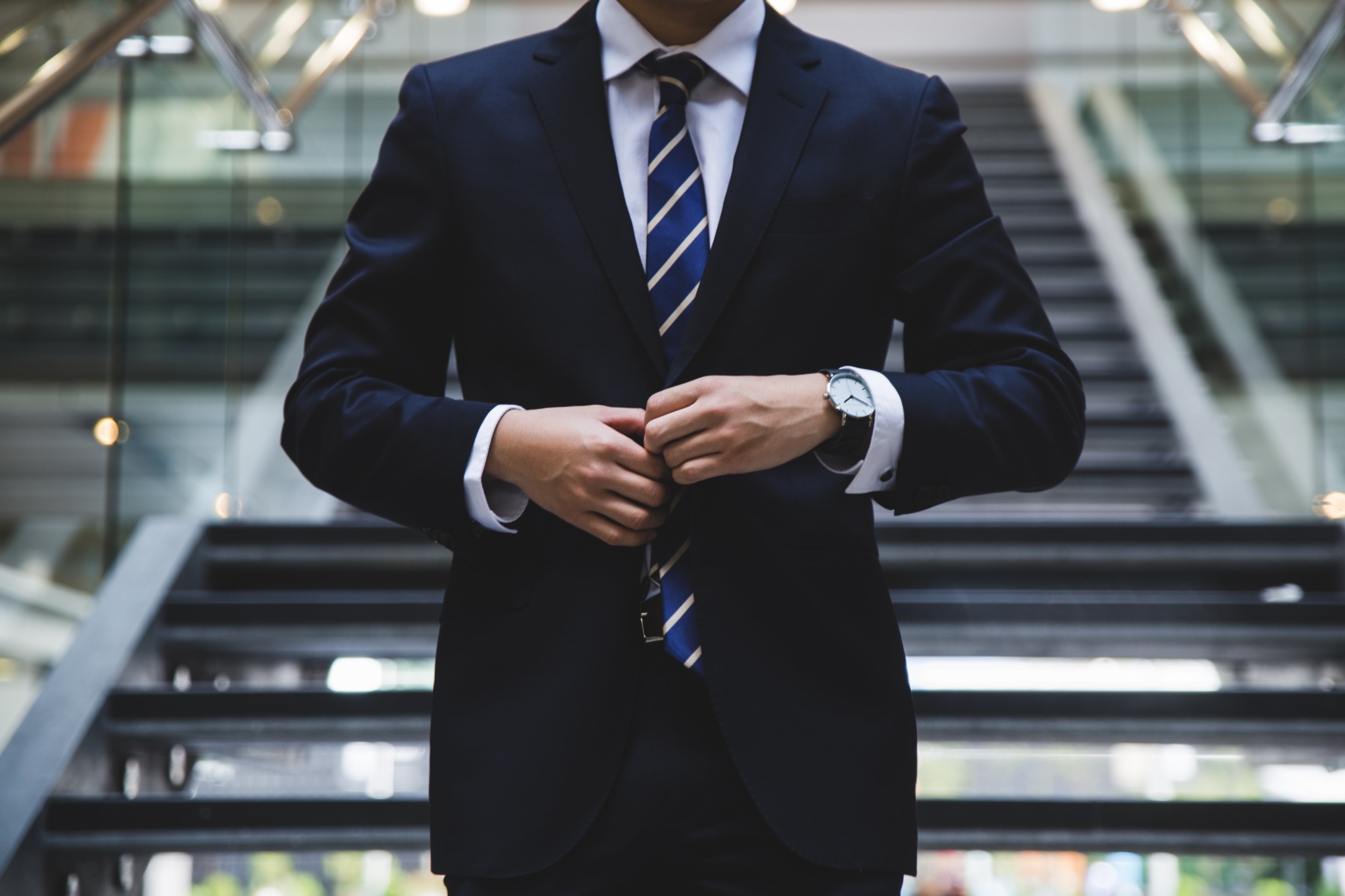 A person standing near the stairs buttoning up a suit jacket.