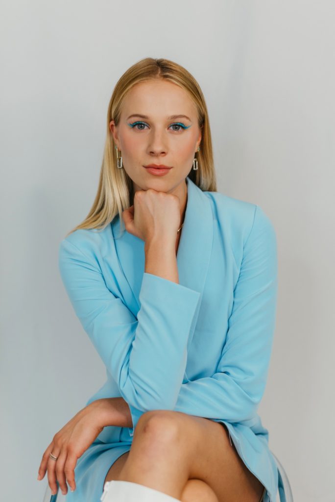 emma oleck sitting in a blue blazer with her legs crossed