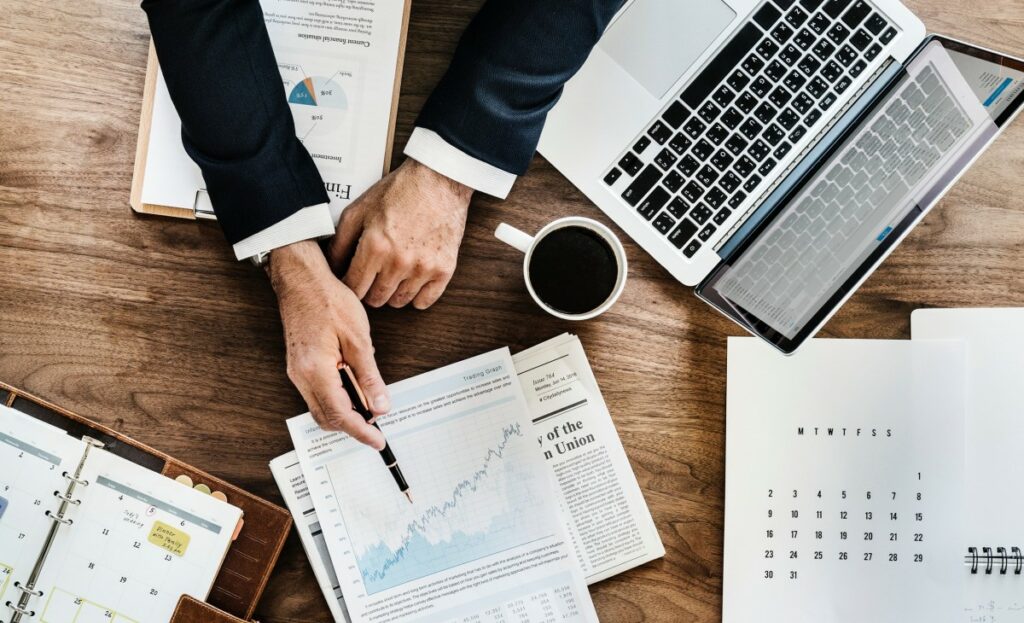 Photo of a businessman pointing at a spreadsheet with papers around his desk. 