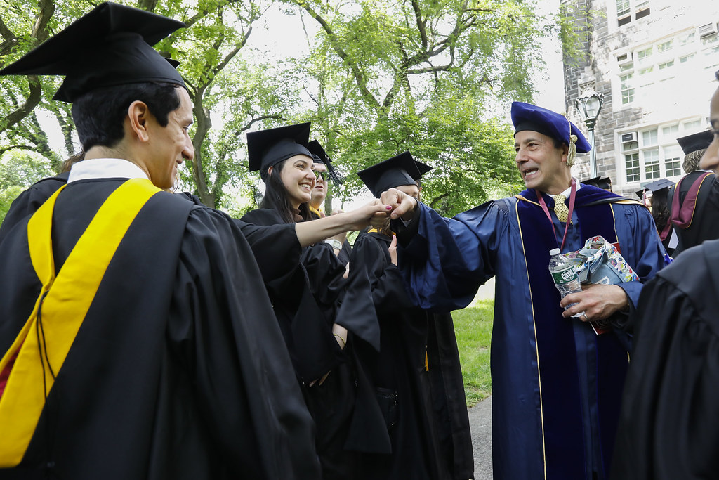 Photo of a college official and recently graduated students all dressed in their caps and gowns