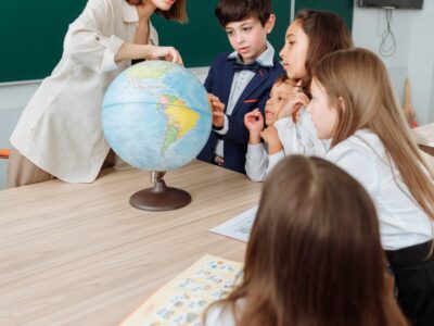 An education major teacher pointing to a globe with students around her.