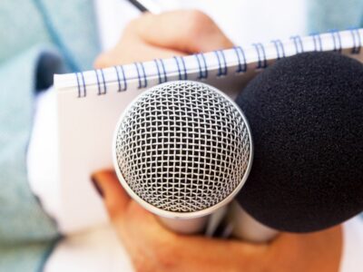 A close up image of a journalist holding onto a microphone and writing in a notepad