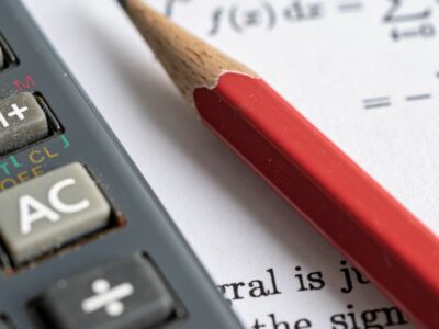 A close up image of a calculator next to a red pencil with a math equation on the background