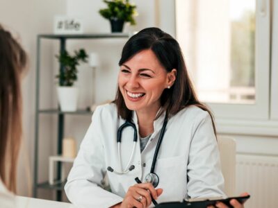 A doctor wearing a lab coat and stethoscope smiling at a patient