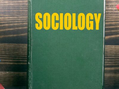 A green book up against a wooden wall with the word sociology written across it in yellow